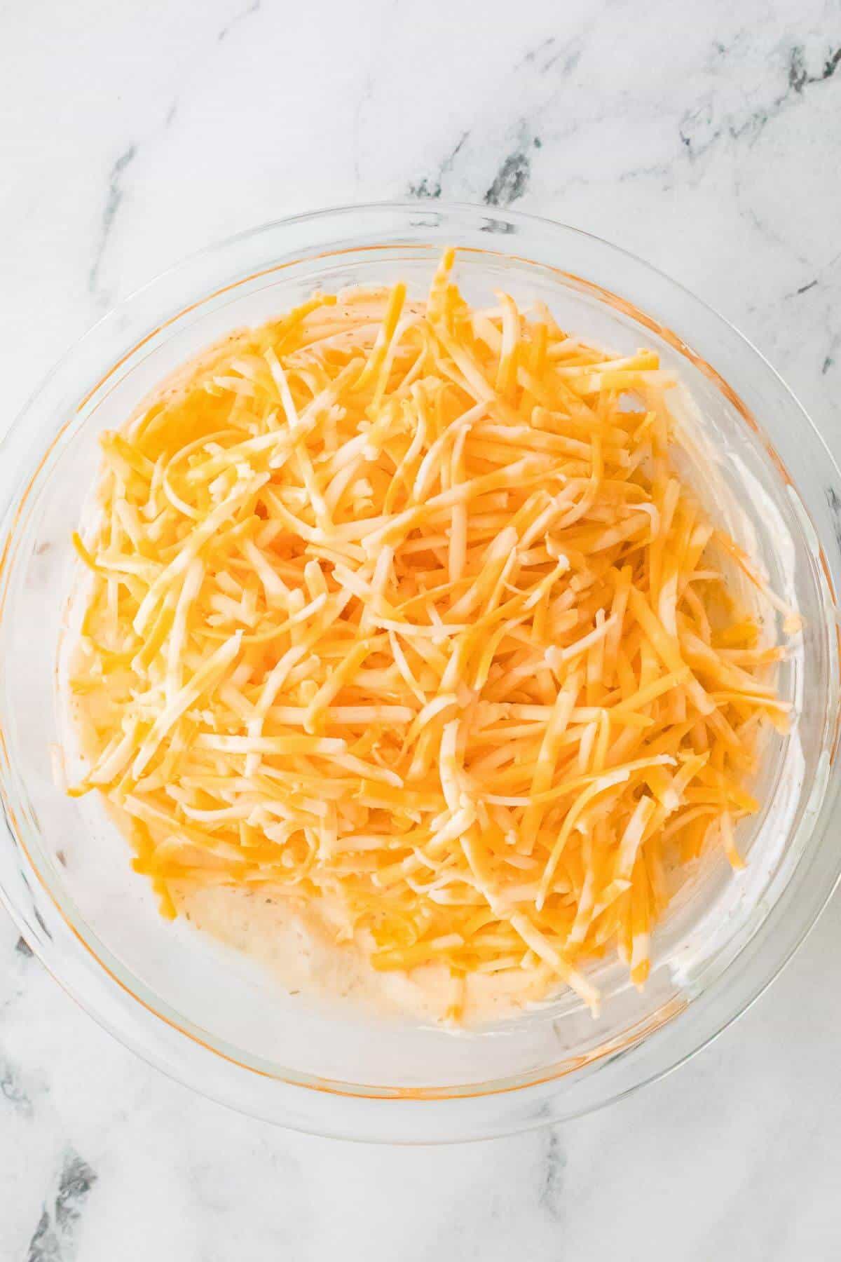 A glass bowl filled with shredded cheese on a marble countertop.