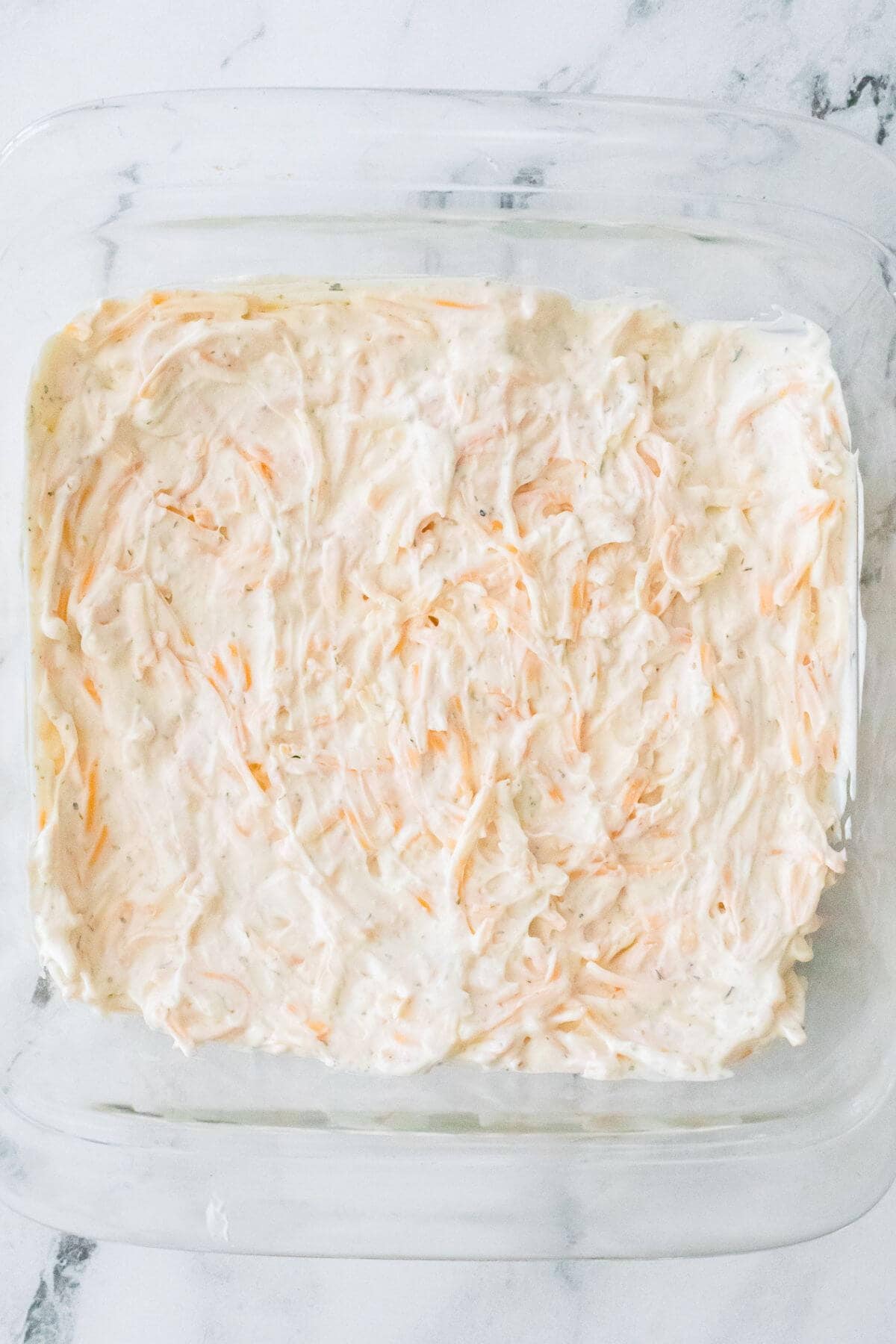 A glass baking dish filled with creamy, shredded carrot salad on a marble surface.