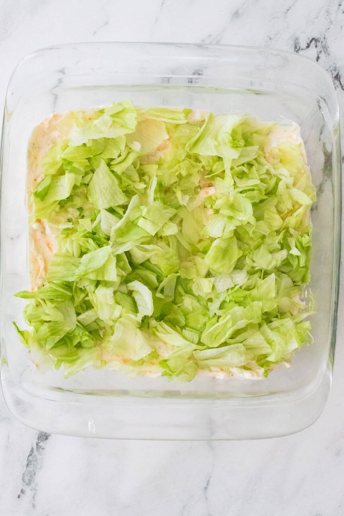 A glass dish filled with layered lettuce on top of a creamy mixture.