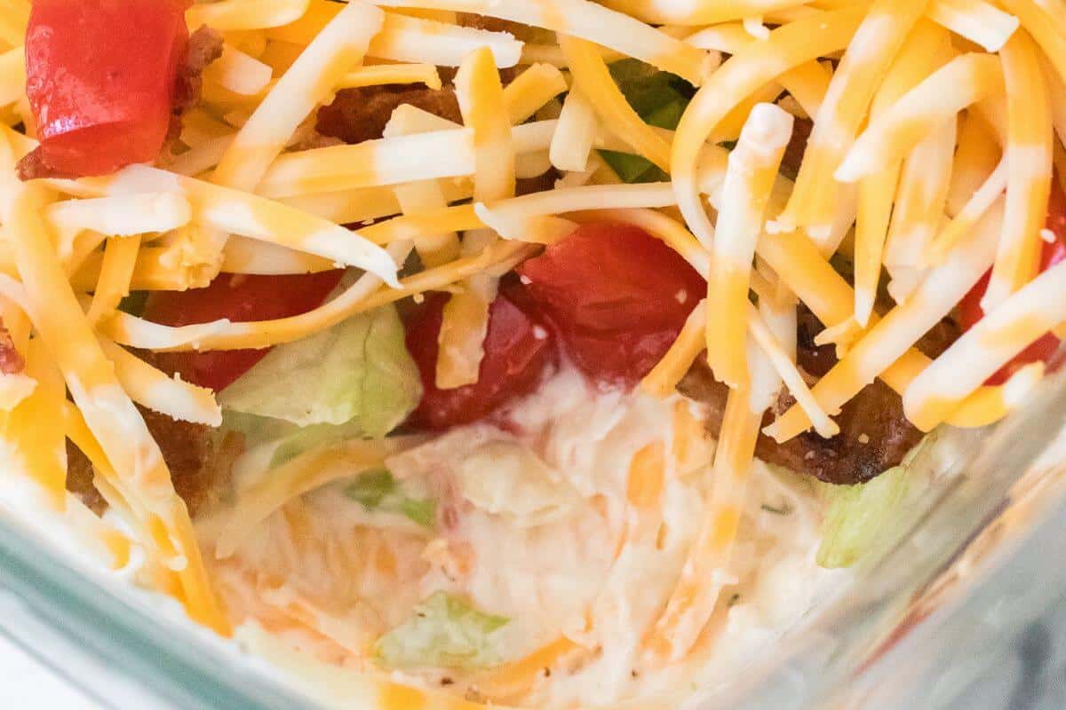 Close-up of a layered salad in a glass container featuring shredded cheese, diced tomatoes, and lettuce.
