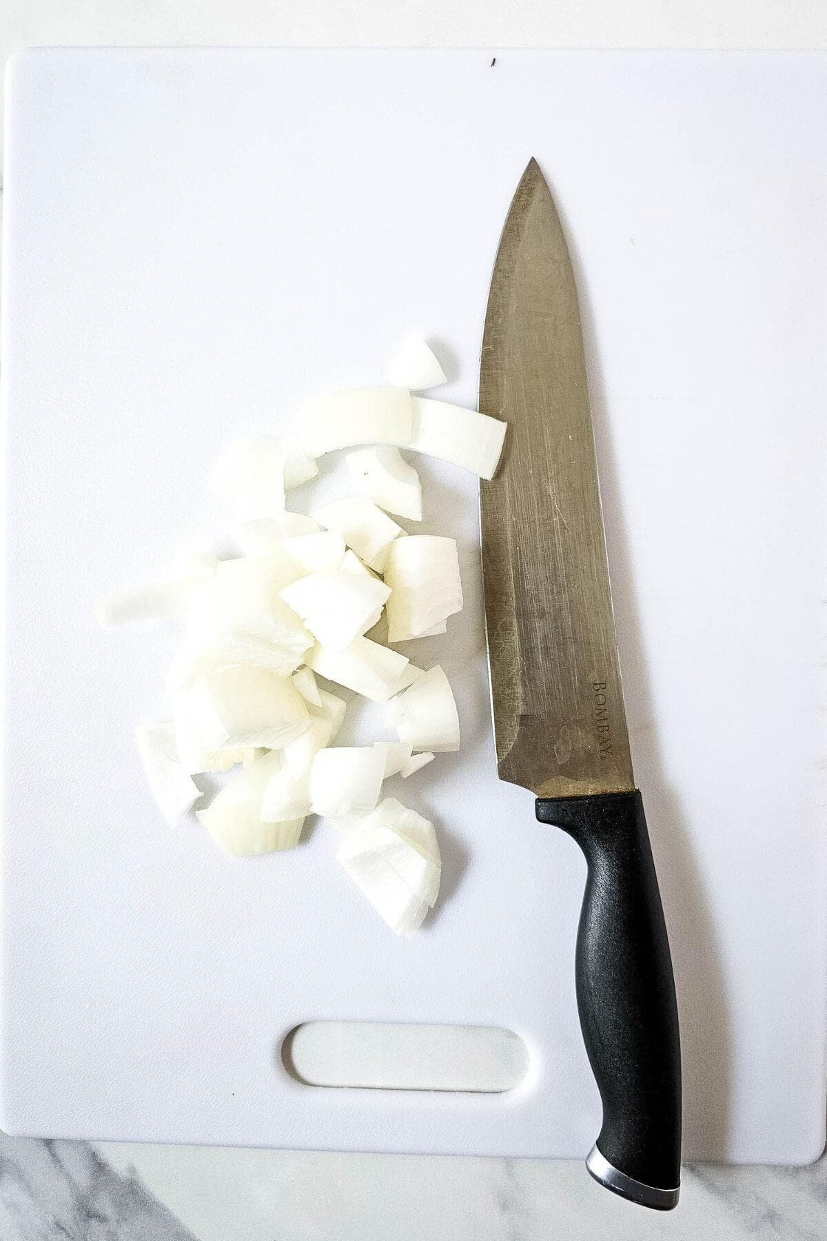 Chopped onions and a large knife on a white cutting board.