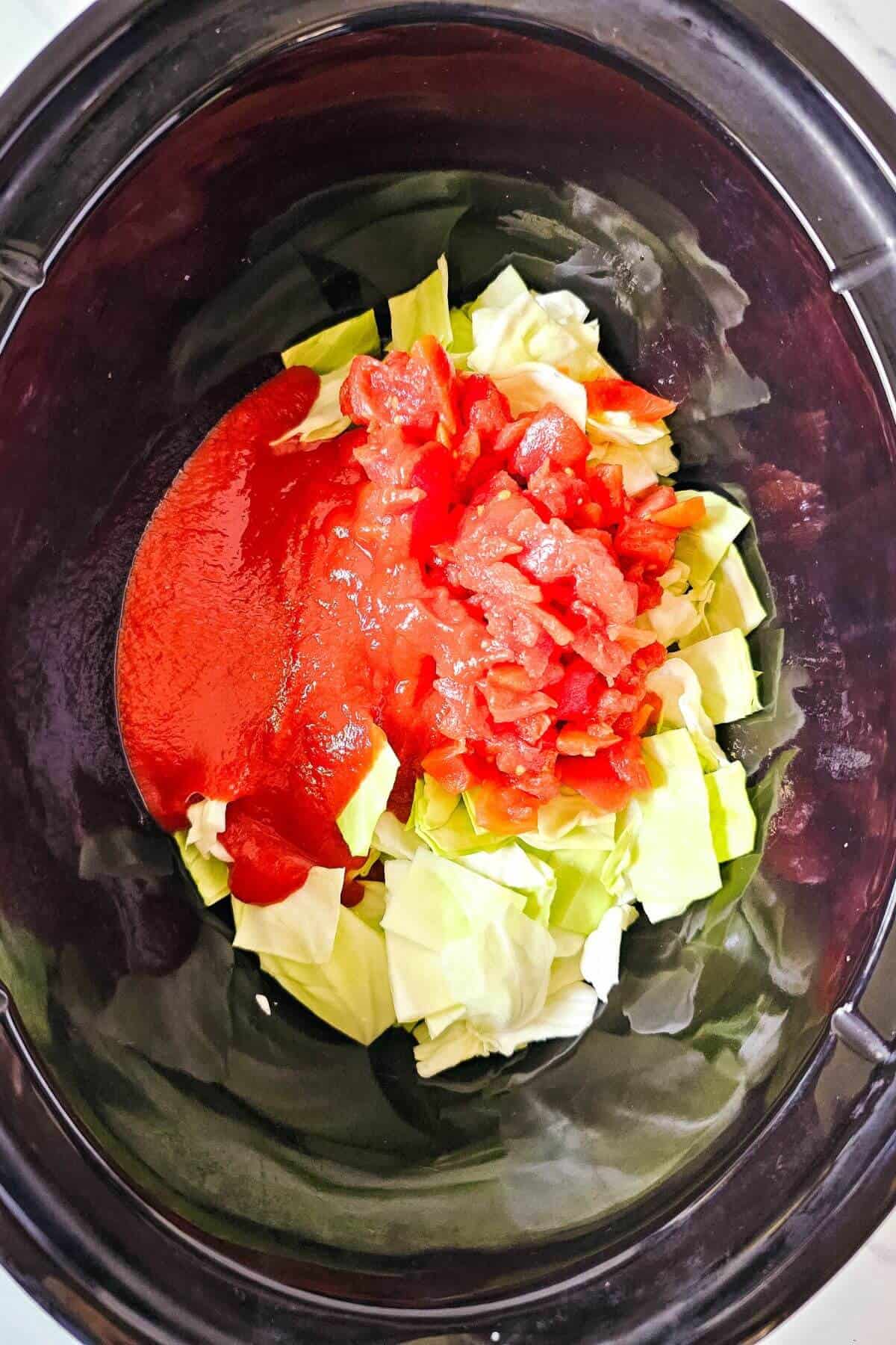 Chopped cabbage and diced tomatoes with sauce in a black crock pot.
