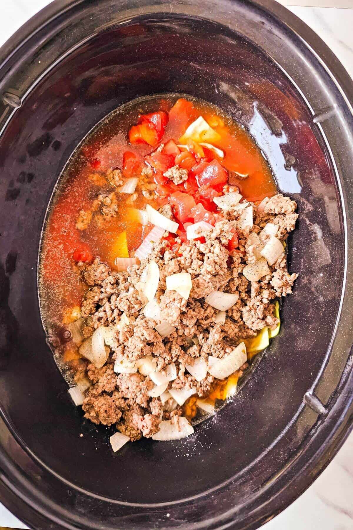 Ground beef, chopped onions, and diced tomatoes in a slow cooker with broth.
