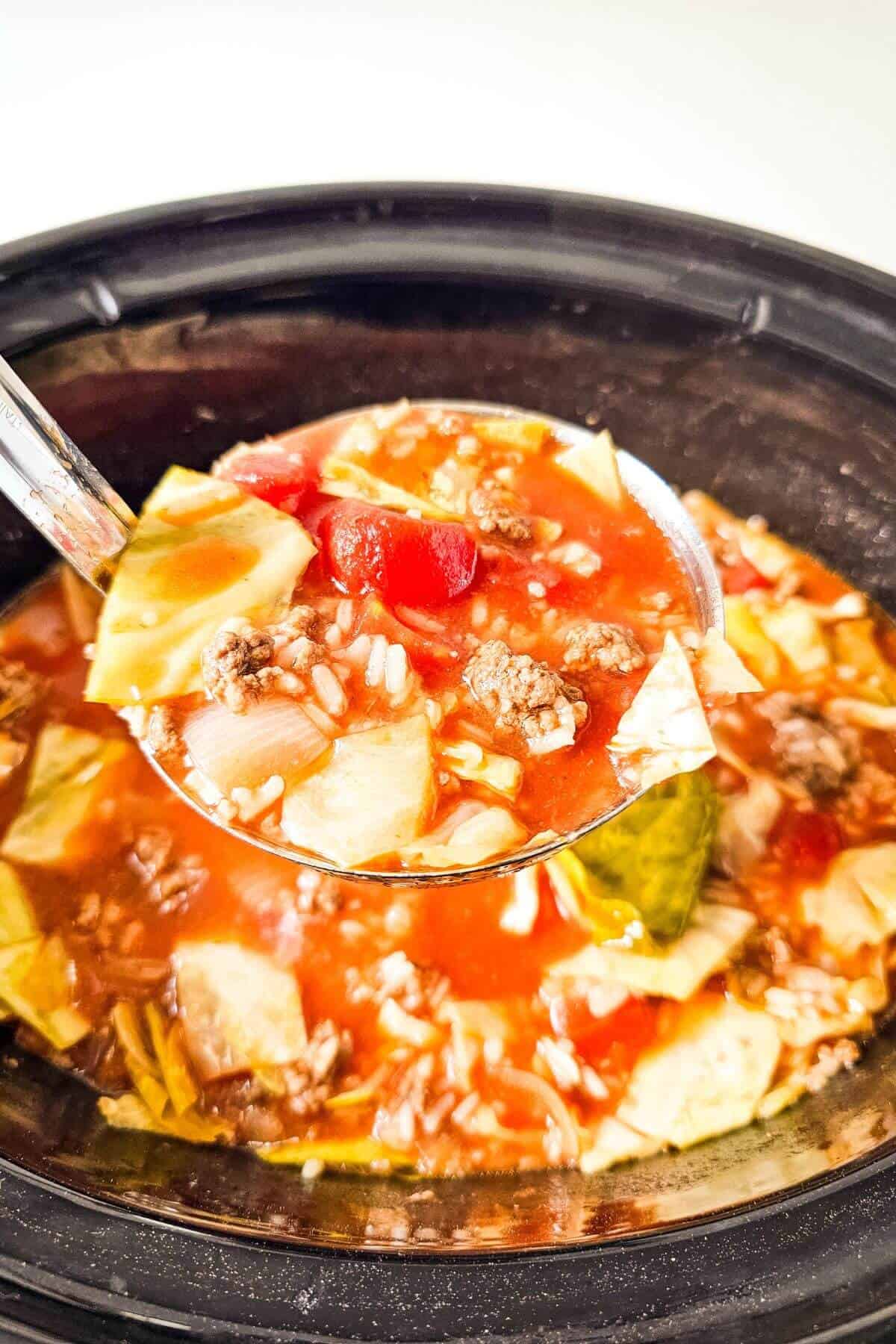 A spoonful of soup with diced tomatoes, ground meat, rice, and cabbage held above a pot filled with the same ingredients.