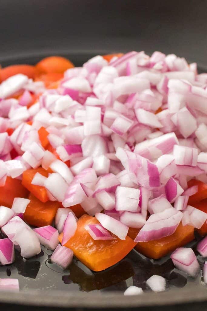 Chopped red onions and tomatoes piled in a black pan.