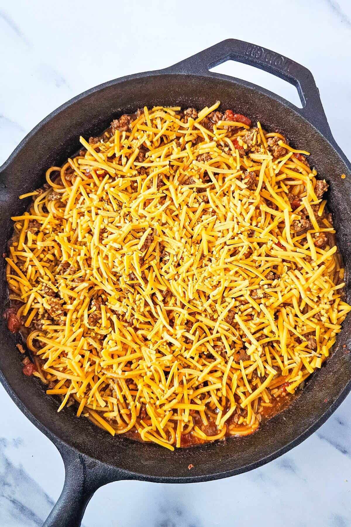 A skillet filled with a cheesy pasta dish, featuring ground meat and shredded cheese on top.