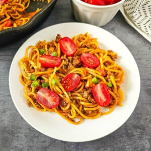 Plate of spaghetti with ground meat, sliced cherry tomatoes, and green onions.
