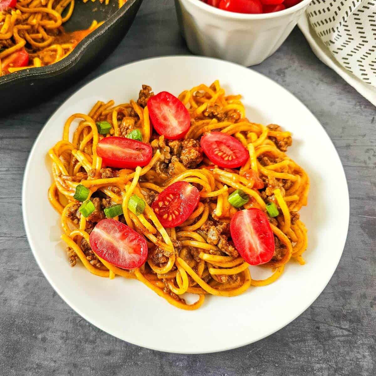 Plate of spaghetti with ground meat, sliced cherry tomatoes, and green onions.