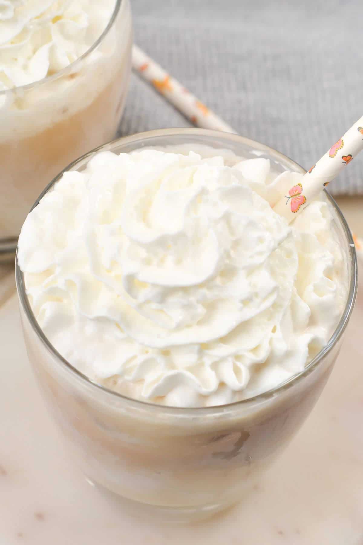 A glass brimming with creamy iced white chocolate mocha, crowned with a swirl of whipped cream and elegantly finished with a decorative straw.