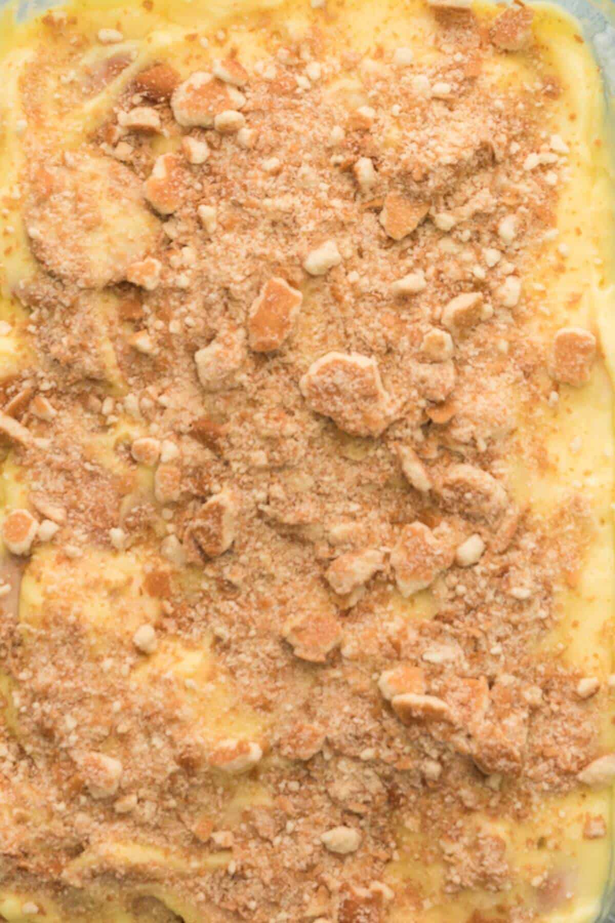 Close-up of a dessert with a crumbly topping, featuring a creamy yellow surface with chunks and crumbs scattered throughout.