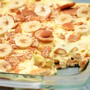 A glass dish of banana pudding topped with banana slices and crushed cookies.