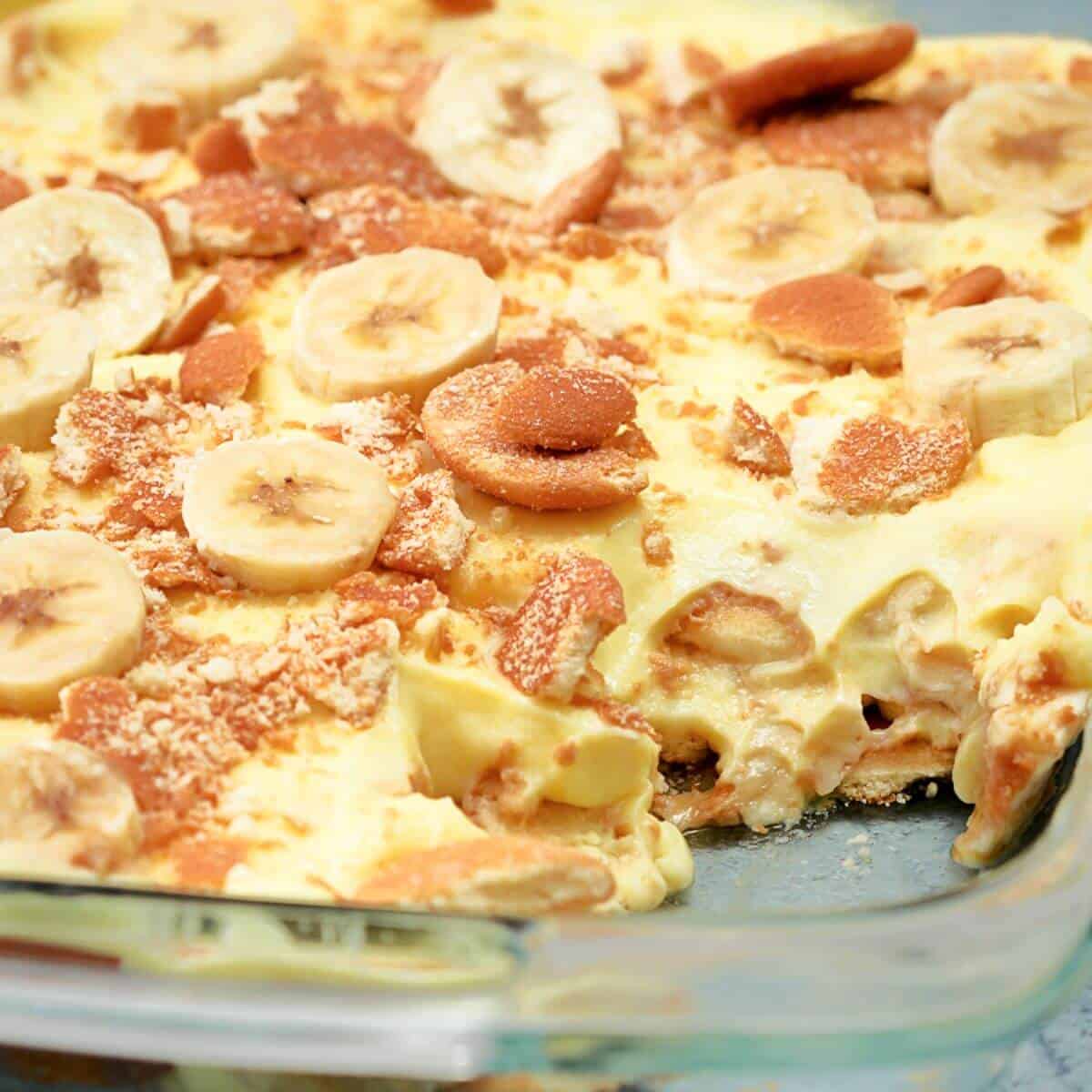 A glass dish of banana pudding topped with banana slices and crushed cookies.