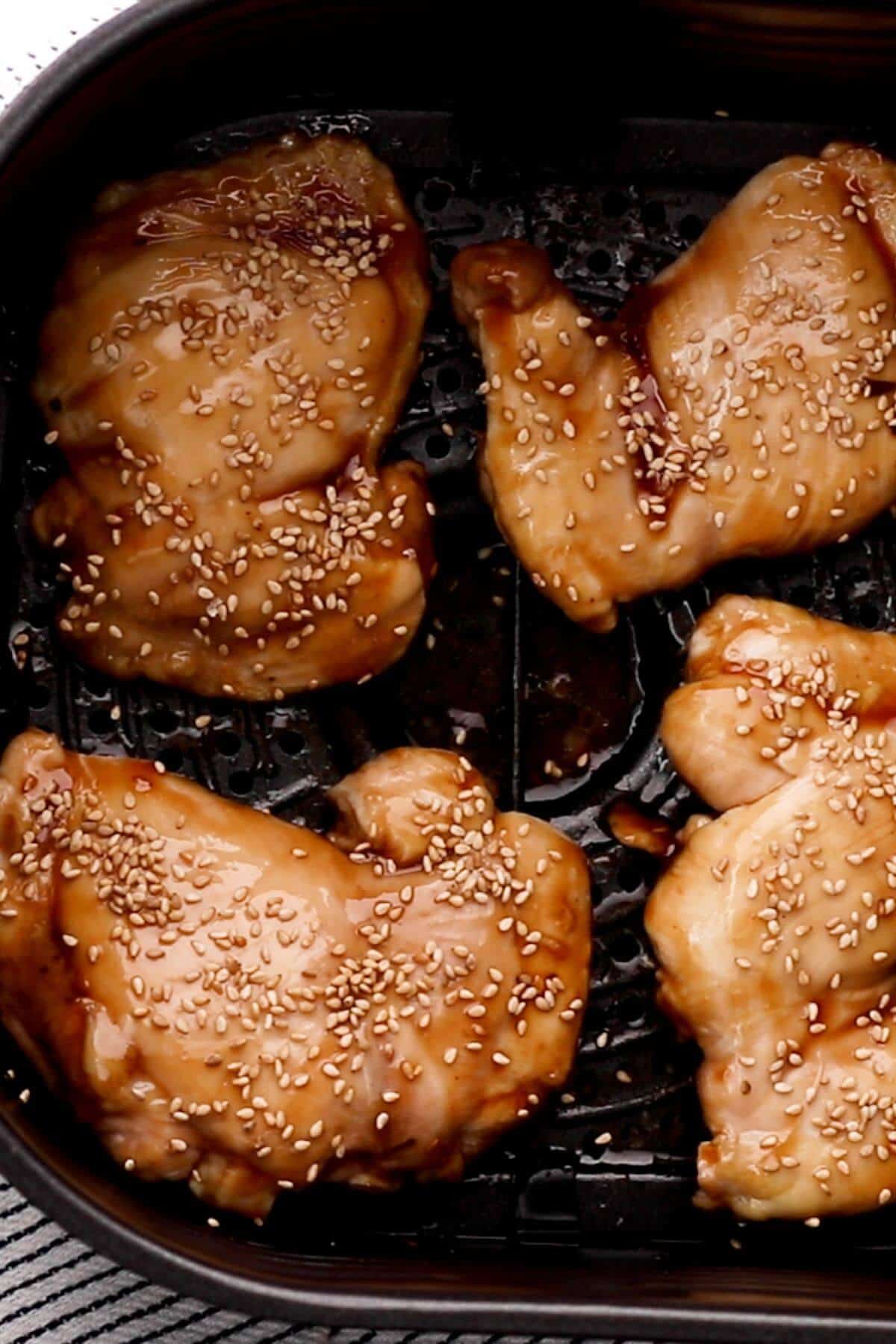 Four pieces of glazed chicken garnished with sesame seeds in an air fryer basket.