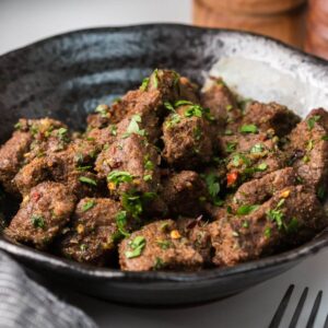 A bowl of spiced, roasted meat cubes garnished with chopped herbs.