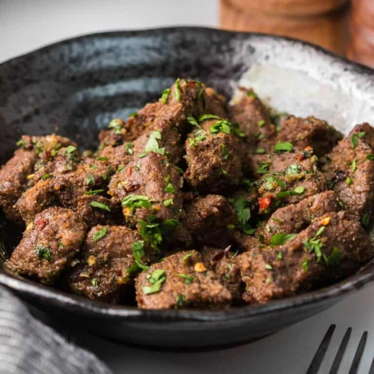 A bowl of spiced, roasted meat cubes garnished with chopped herbs.