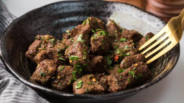 A bowl of seasoned meat cubes garnished with chopped herbs, with a fork resting on the side.