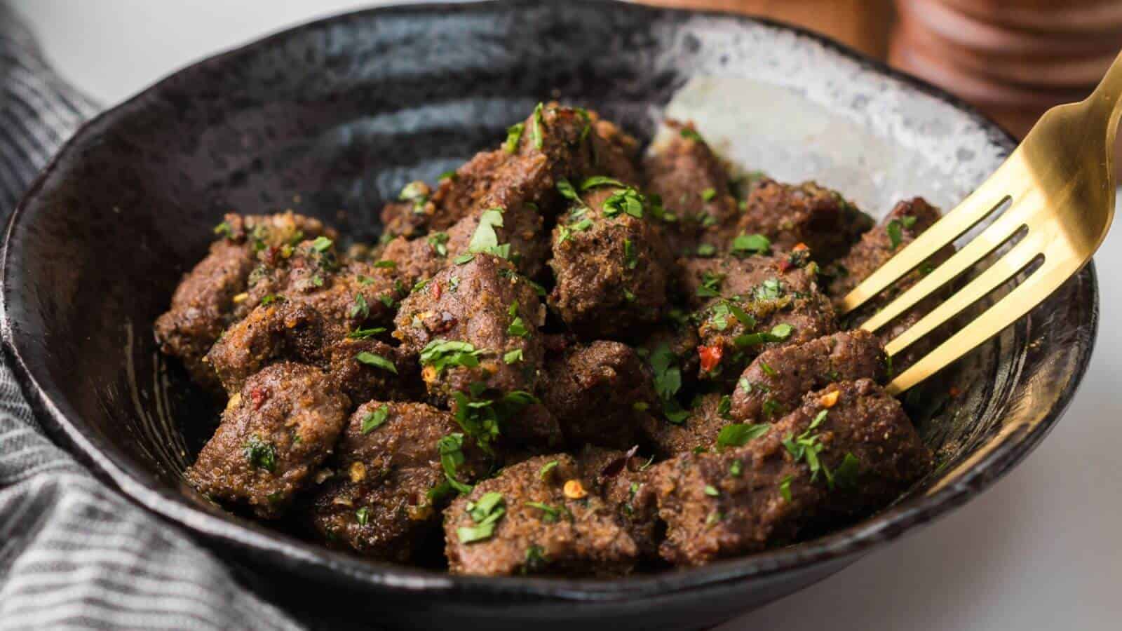 A bowl of seasoned meat cubes garnished with chopped herbs, with a fork resting on the side.