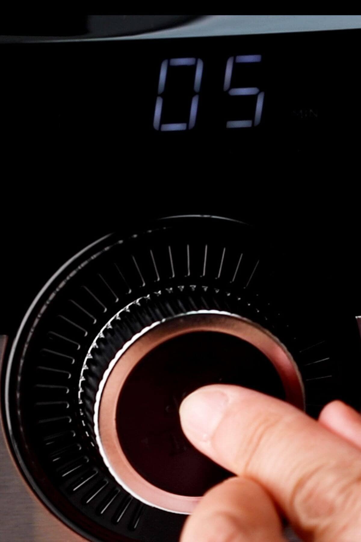 Close-up of a hand adjusting a digital timer knob set to 05 minutes.