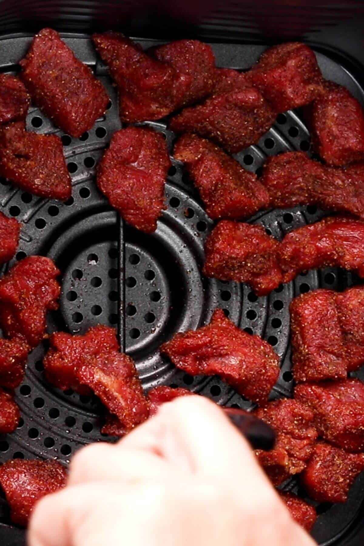 Chunks of raw beef are evenly placed on an air fryer tray.