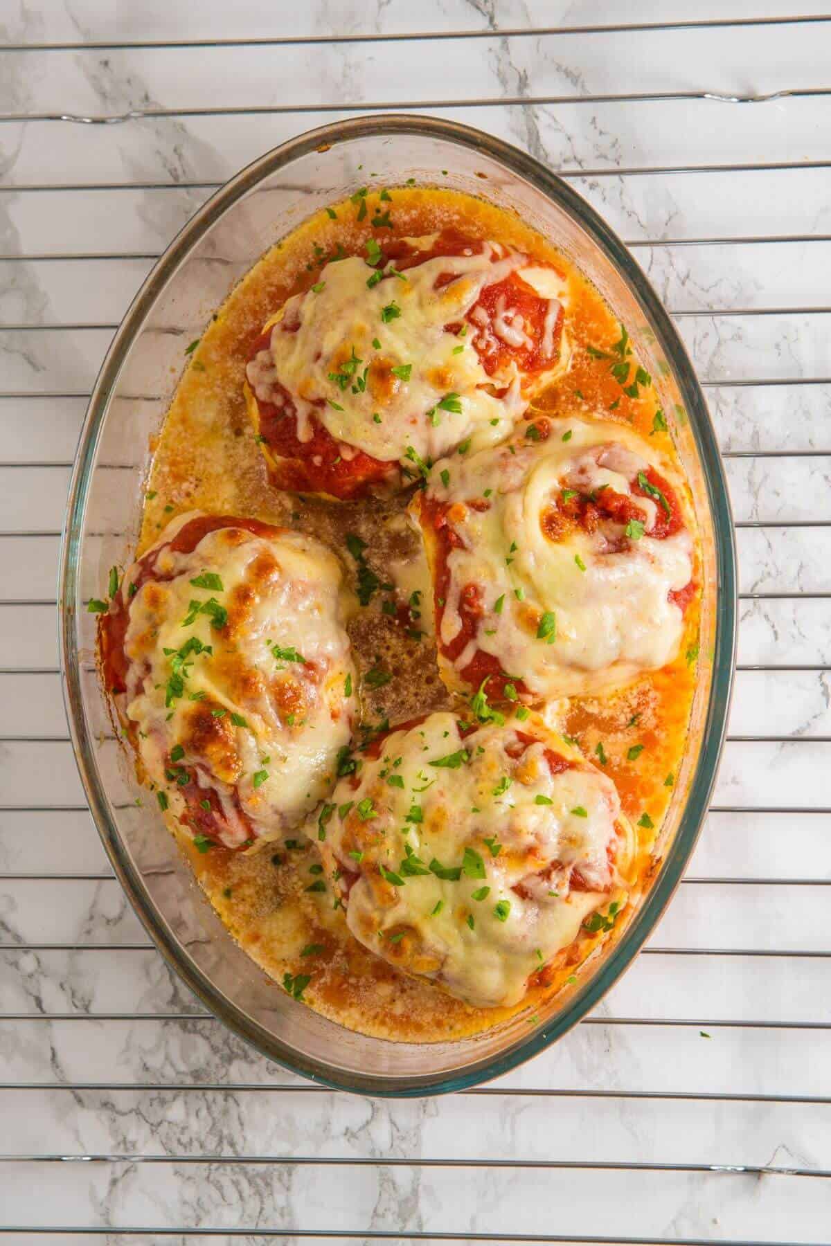 Baked stuffed tomatoes topped with melted cheese and herbs in a glass dish on a striped surface.