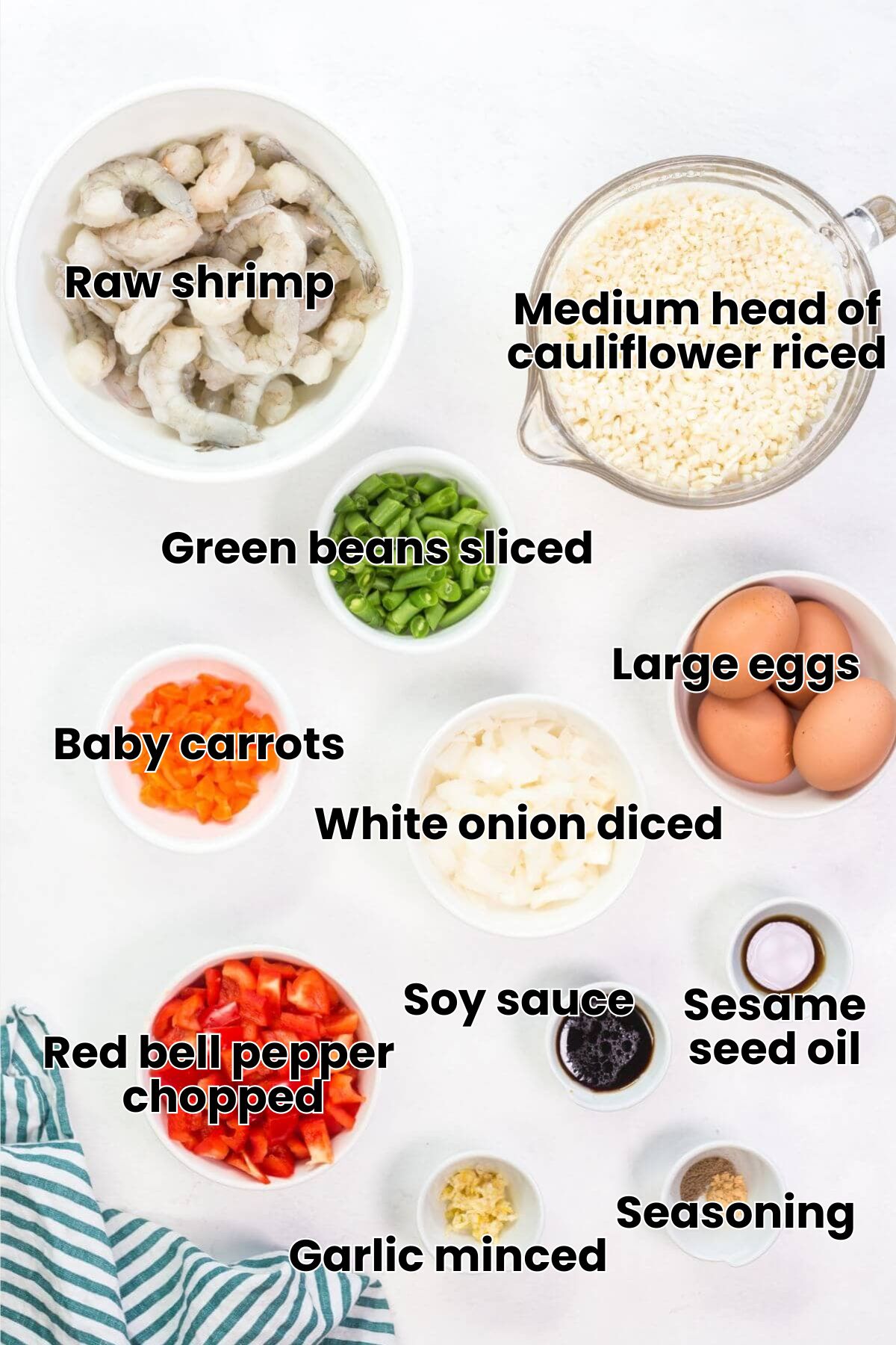 Ingredients for a dish arranged on a table: raw shrimp, rice, green beans, eggs, chopped onions, red bell peppers, garlic, sauces, and seasonings in separate bowls. Striped cloth nearby hints at a delicious keto fried cauliflower rice with shrimp masterpiece waiting to be crafted.