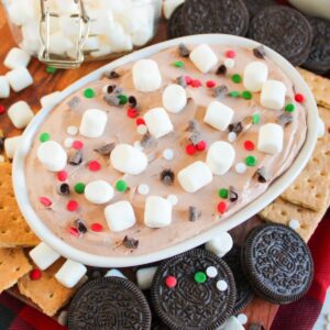A festive dessert dip topped with mini marshmallows, chocolate chips, and sprinkles in a dish. Surrounded by cookies and graham crackers.