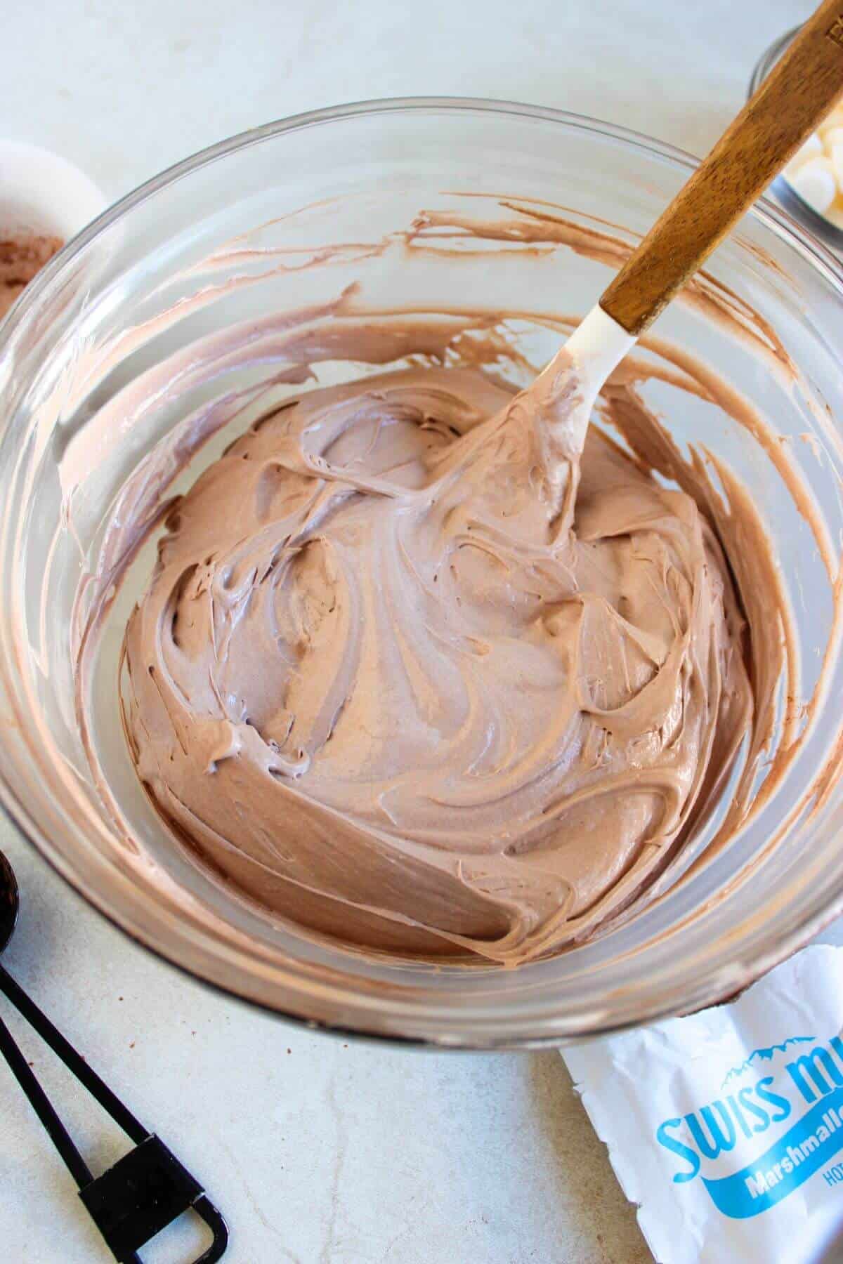 A mixing bowl with creamy chocolate mousse being stirred with a wooden spoon, next to a packet labeled "Swiss Miss.
