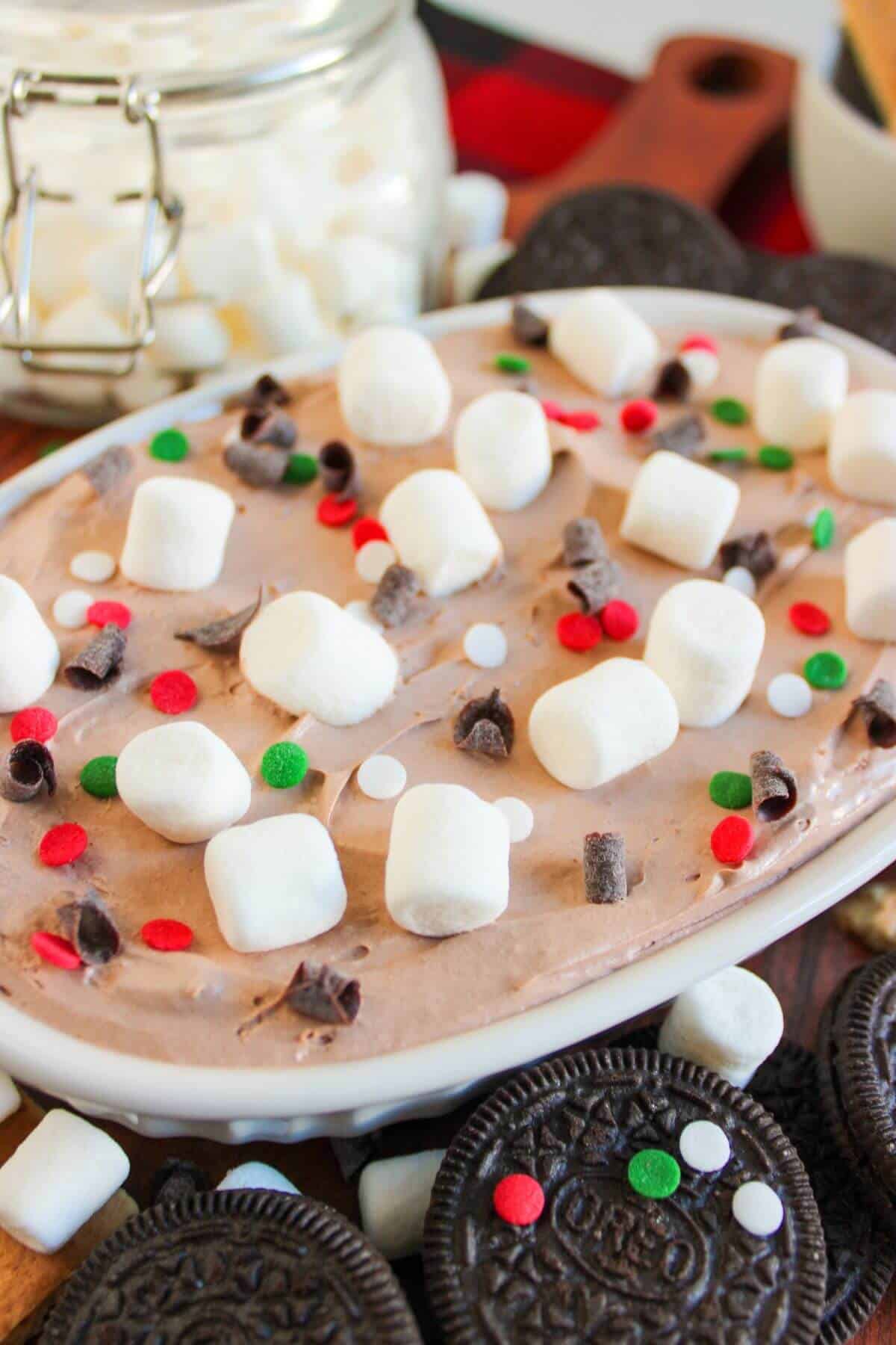 A dessert topped with mini marshmallows, chocolate chips, and red and green sprinkles. Oreo cookies and more marshmallows are scattered around.