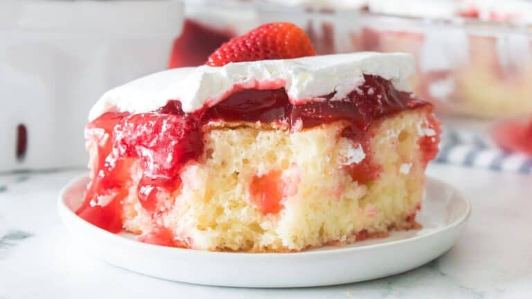 A slice of strawberry poke cake with white frosting and strawberry topping on a white plate.