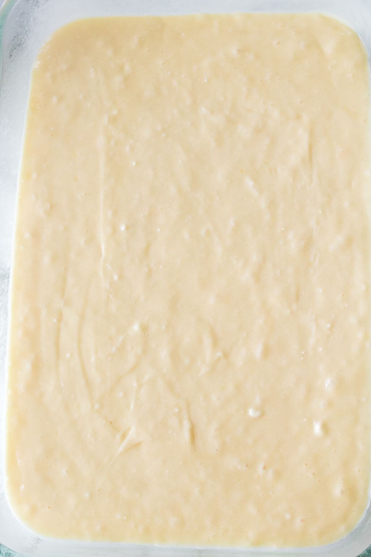 A pale, creamy batter spread evenly in a rectangular glass dish.