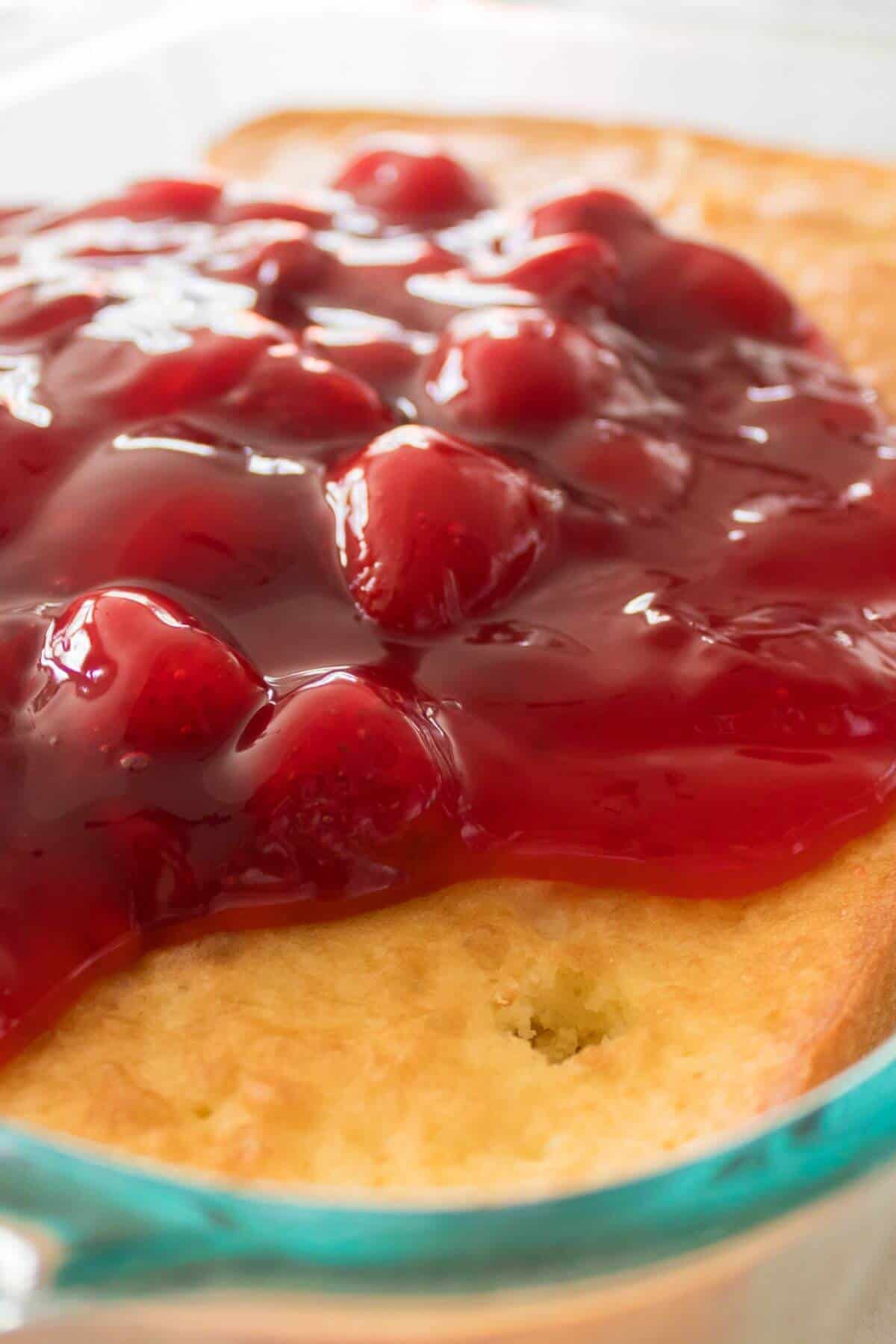 A close-up of a dessert with a golden crust topped with glossy red cherry filling in a glass dish.