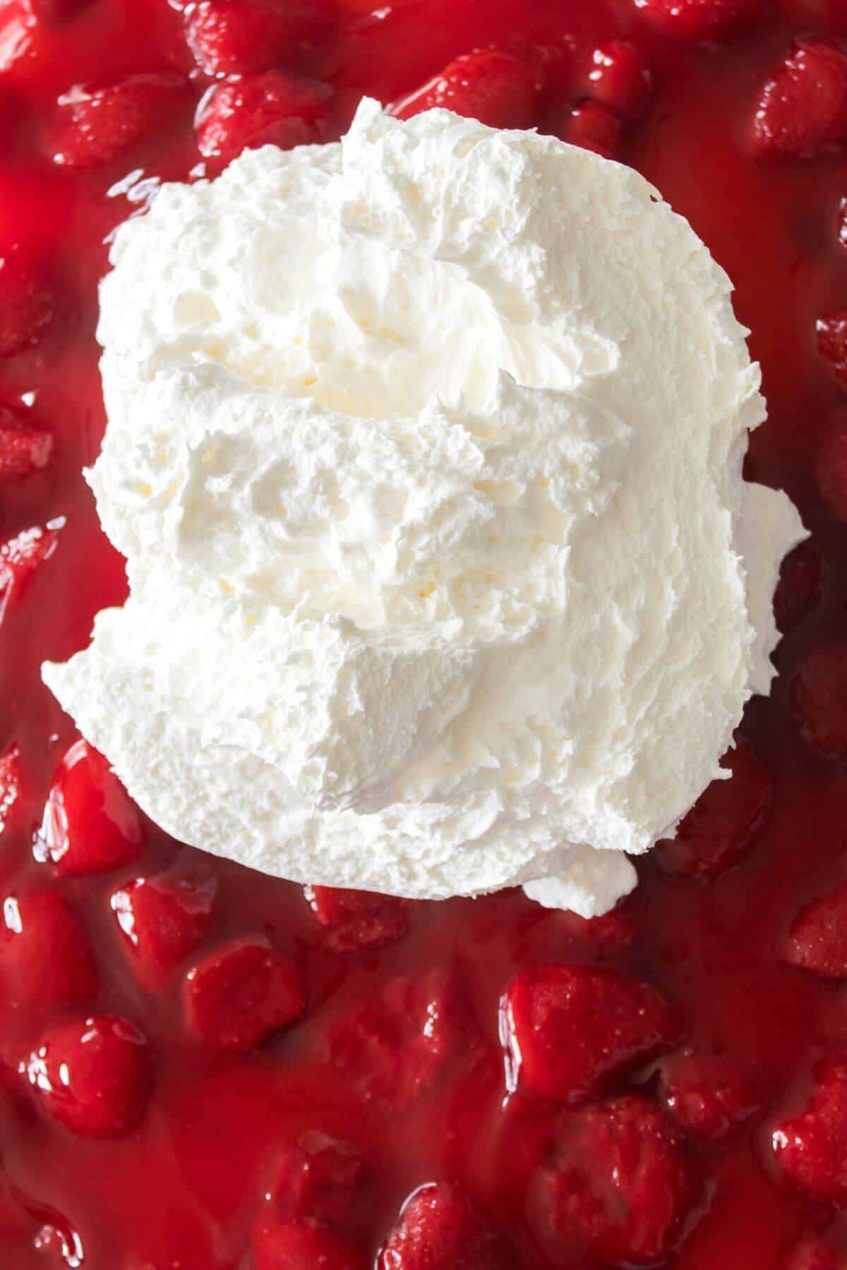 Whipped cream dollop on strawberry sauce with visible chunks of strawberries.