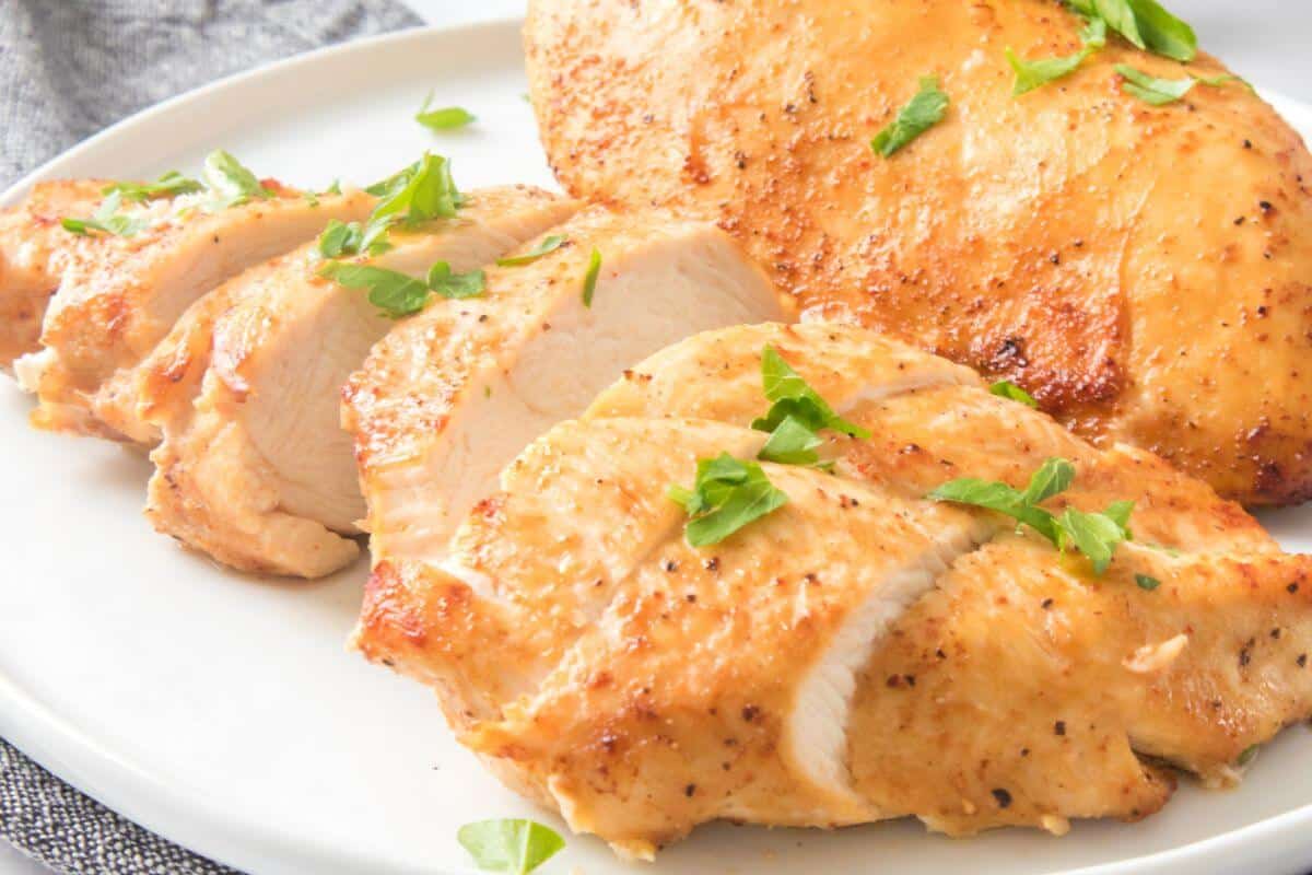Sliced grilled chicken breast garnished with parsley on a white plate.