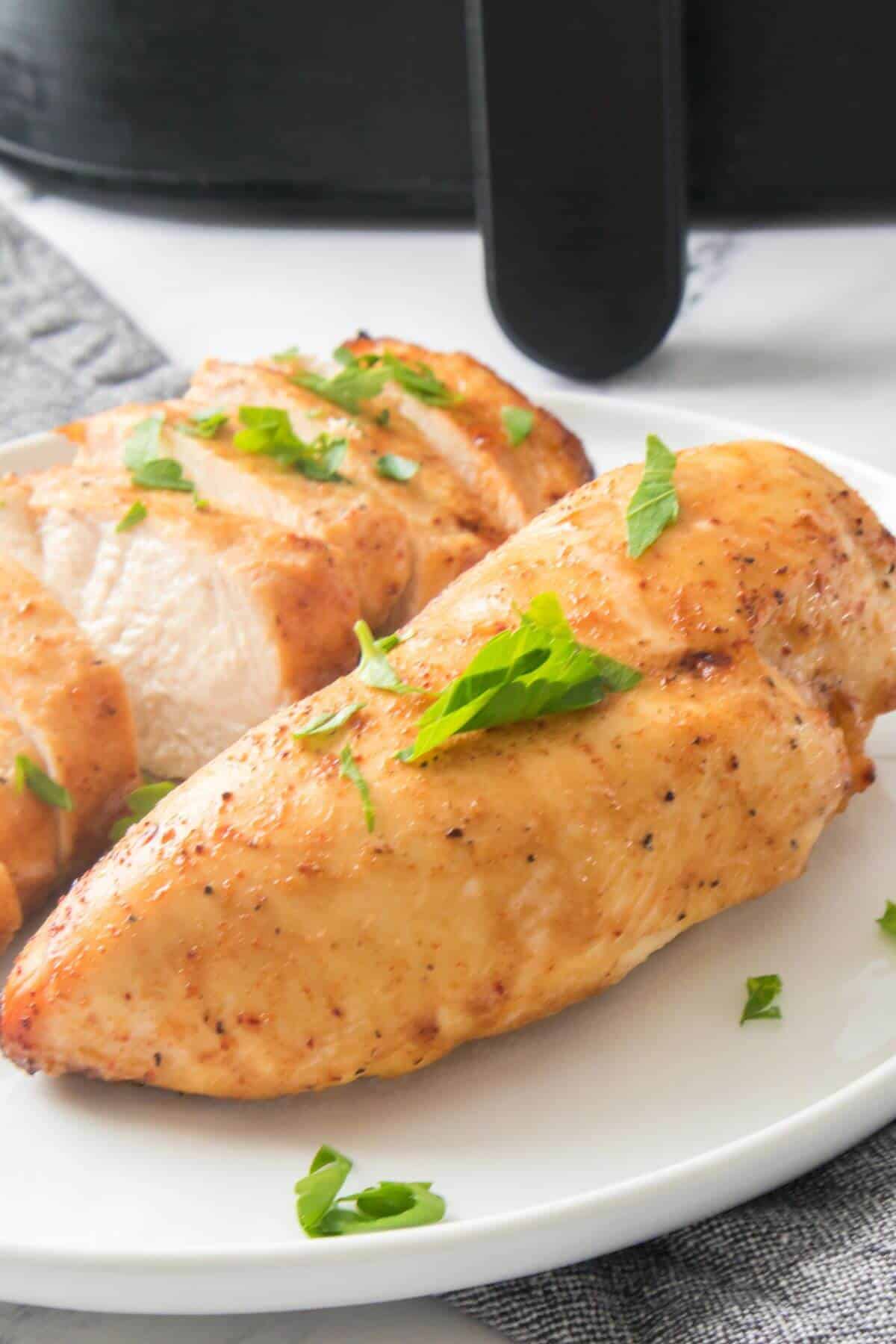 Sliced cooked chicken breast garnished with herbs on a white plate.