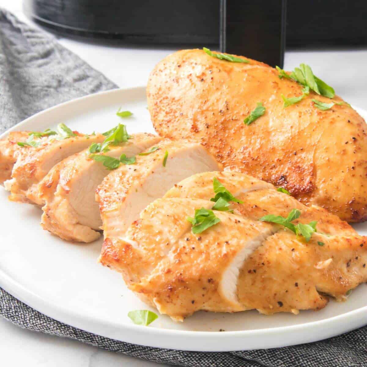 A plate with a whole and sliced cooked chicken breast garnished with herbs.