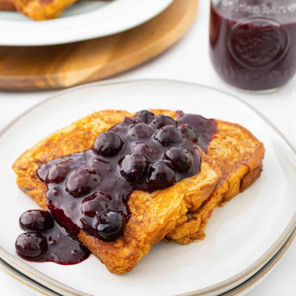 French toast topped with blueberry sauce on a white plate, with a jar of sauce in the background.