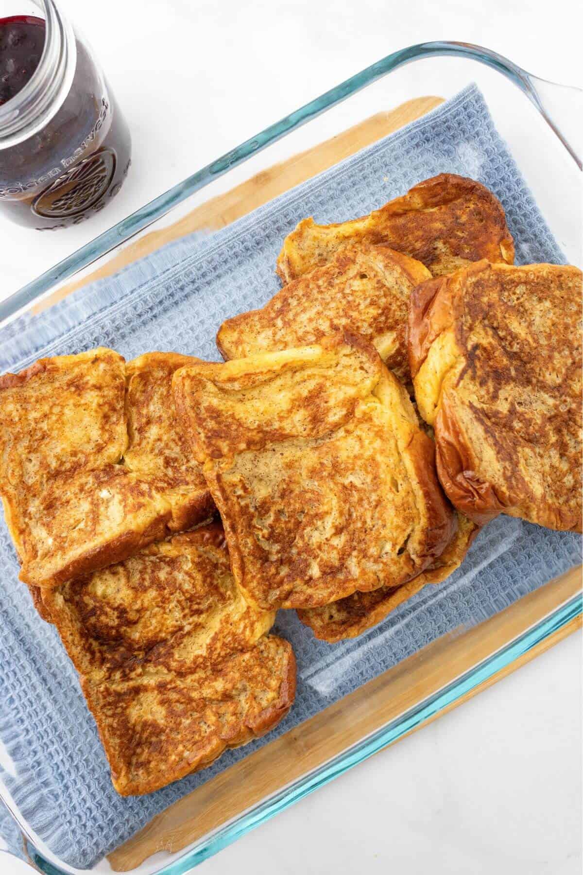 Slices of French toast on a glass baking dish with a jar of jam nearby.