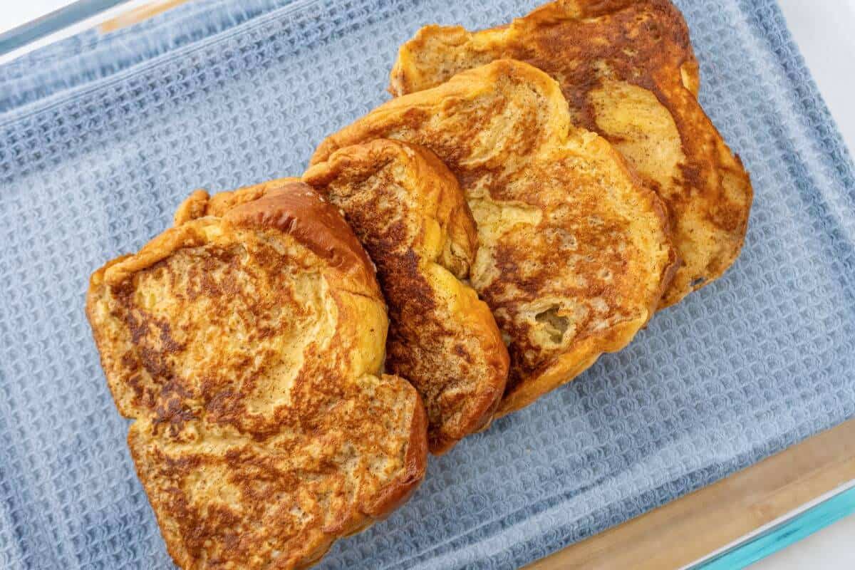 Four slices of golden-brown French toast arranged on a blue textured cloth.