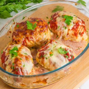Baked stuffed chicken breasts topped with melted cheese and tomato sauce in a glass dish, garnished with parsley.