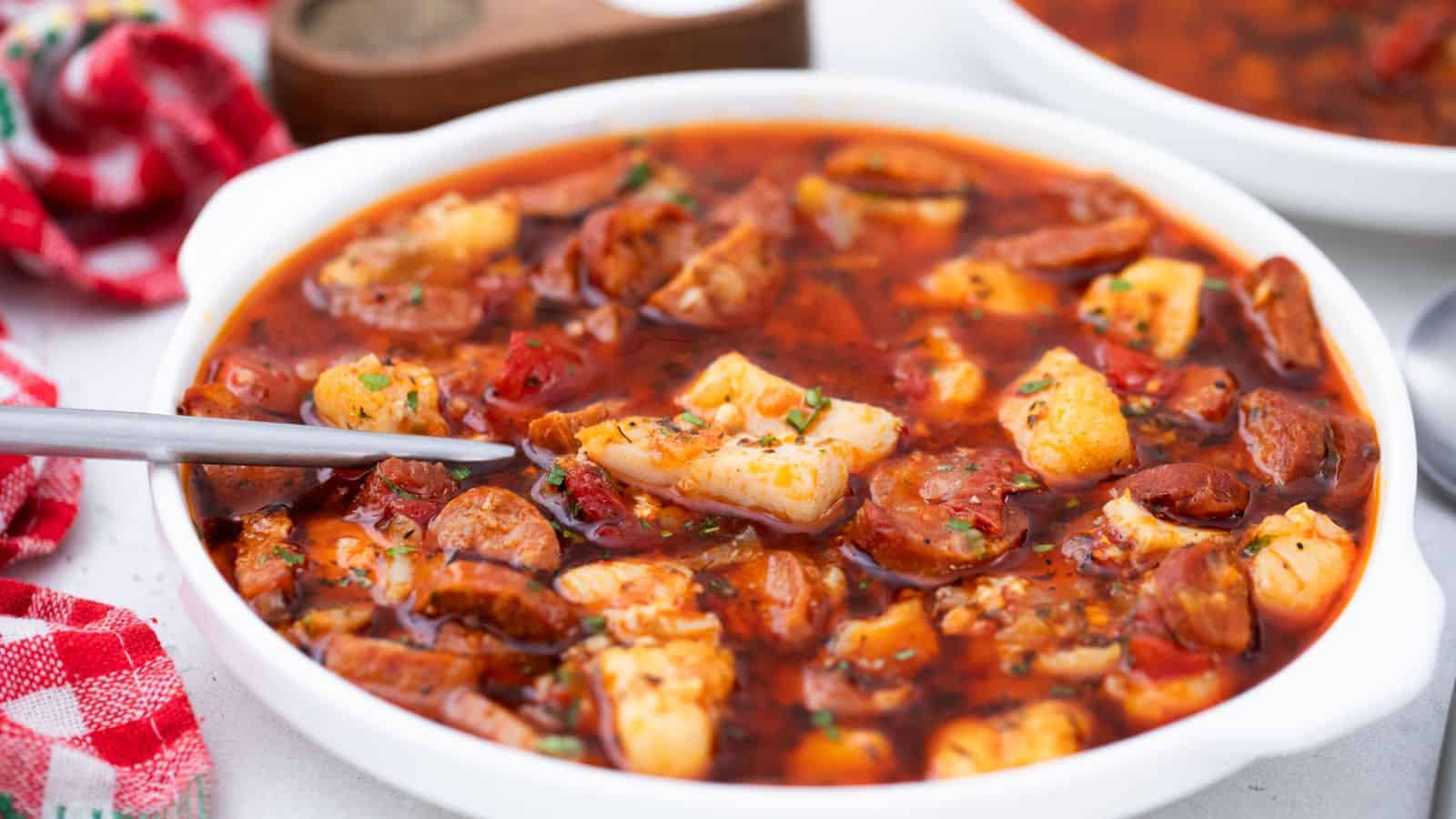 A bowl of soup with sausage and fish.