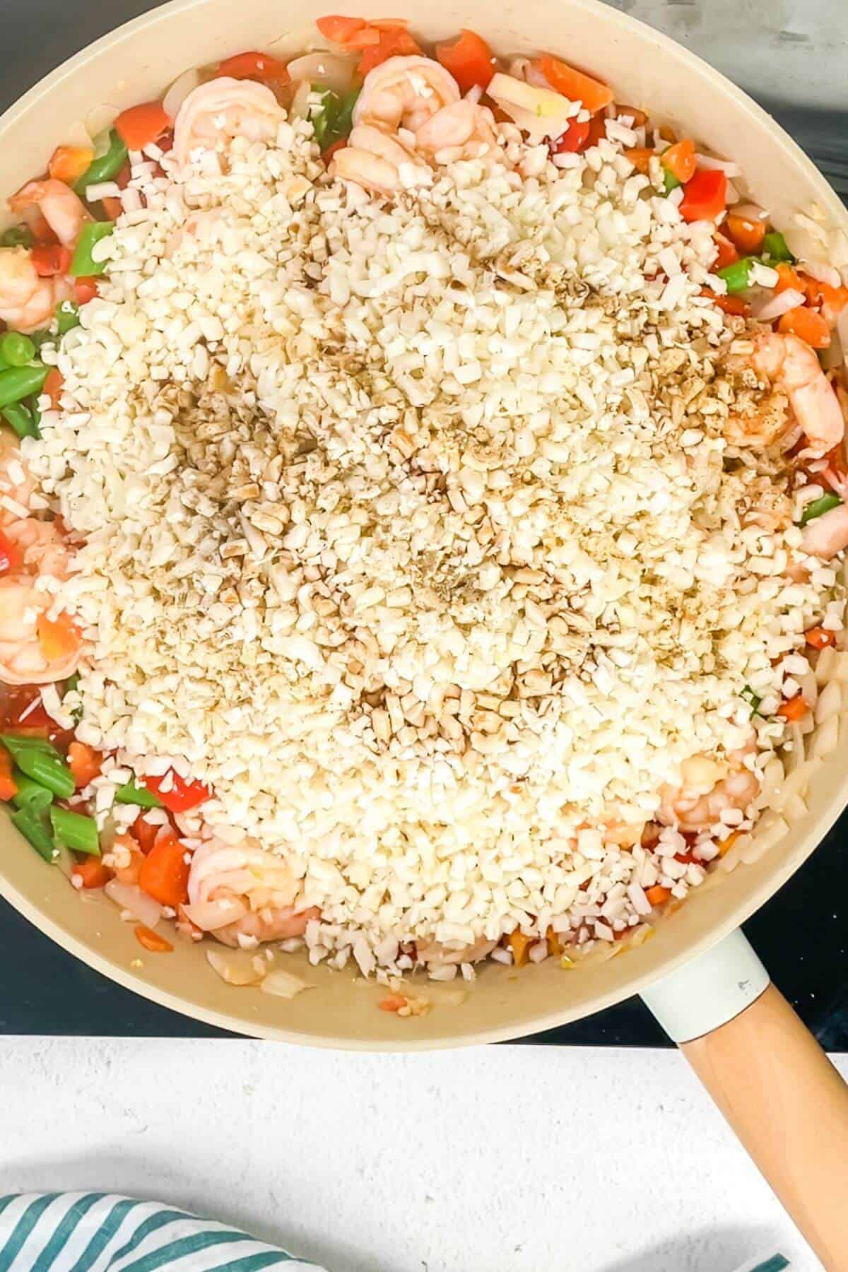 A skillet filled with shrimp, chopped vegetables, and topped with a mound of keto fried cauliflower rice.