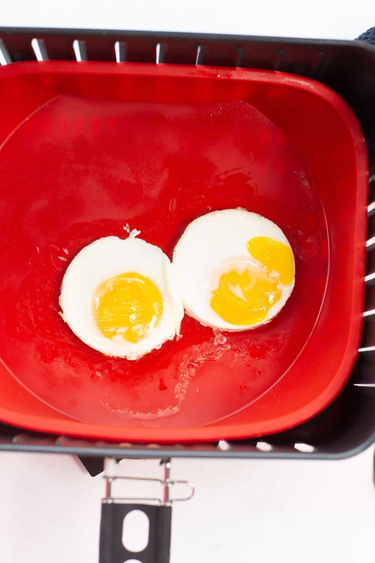 Two poached eggs rest in a red container within the air fryer basket, showcasing the versatility of creating perfect fried eggs in an air fryer.