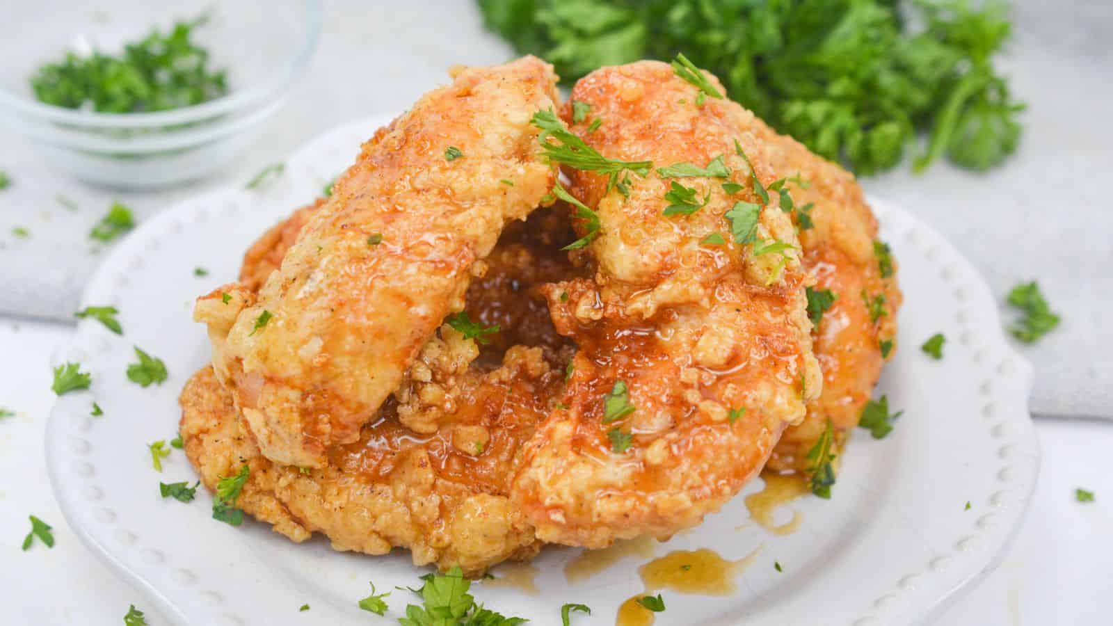 Serving of honey butter chicken garnished with parsley on plate.