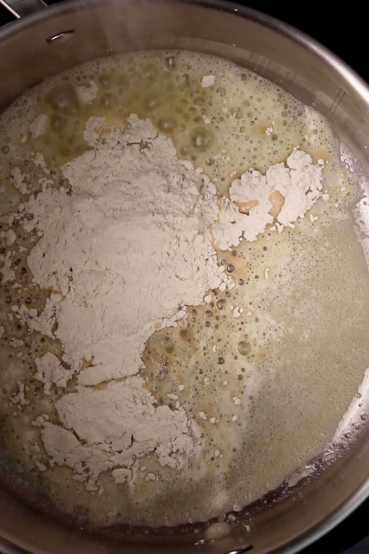 Flour is added to a pot with melted butter, forming a bubbling mixture for a roux.