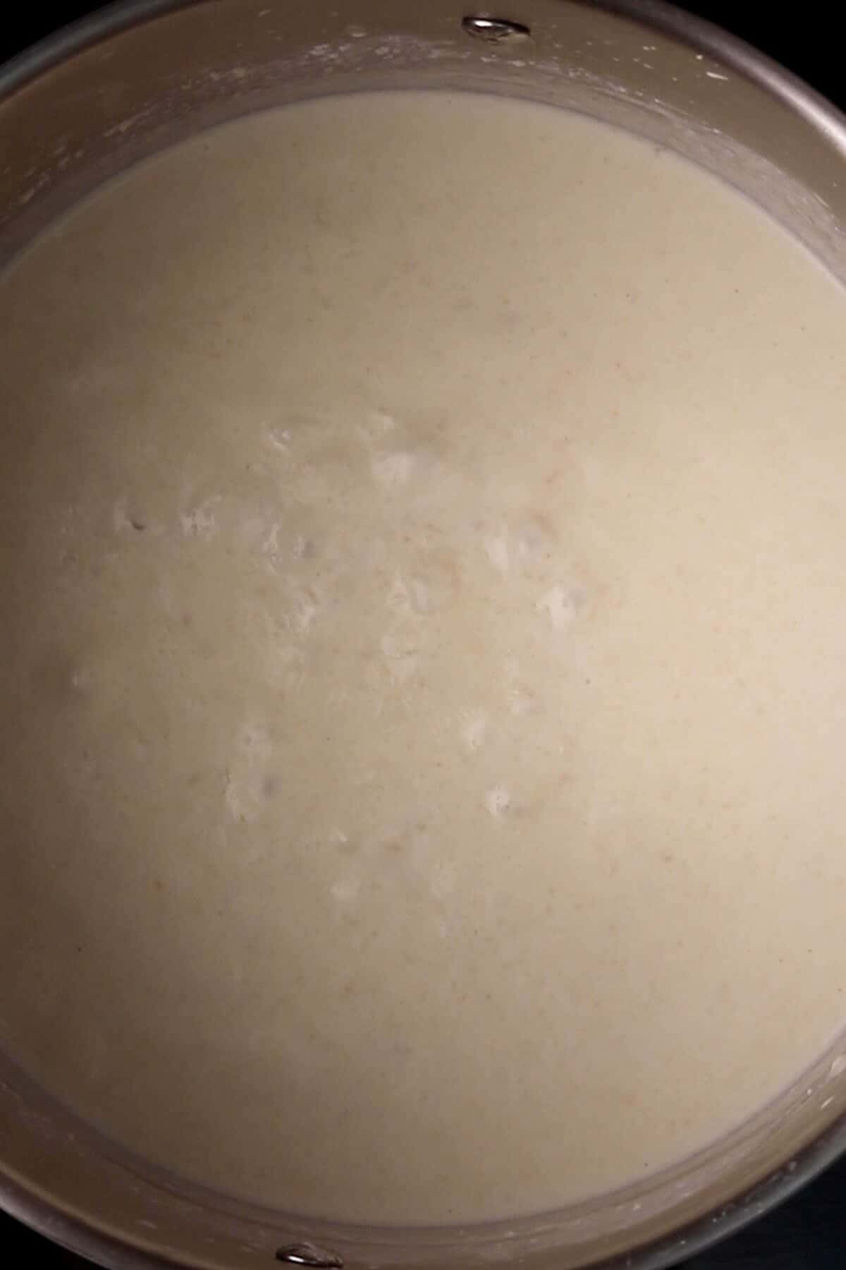 A close-up of a pot filled with creamy, white soup or sauce. Some bubbles are visible on the surface.