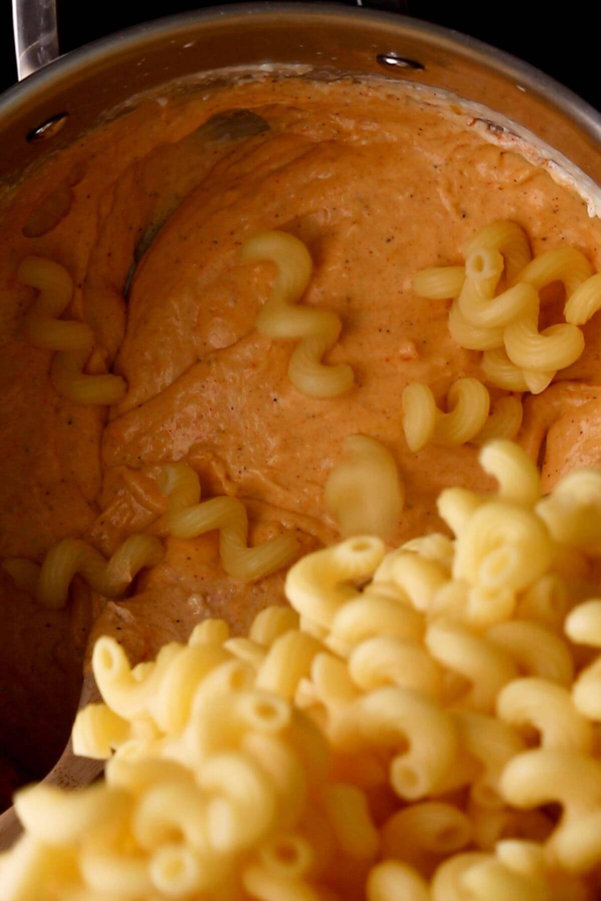 A pot of creamy pasta sauce with partially mixed cooked cavatappi pasta.