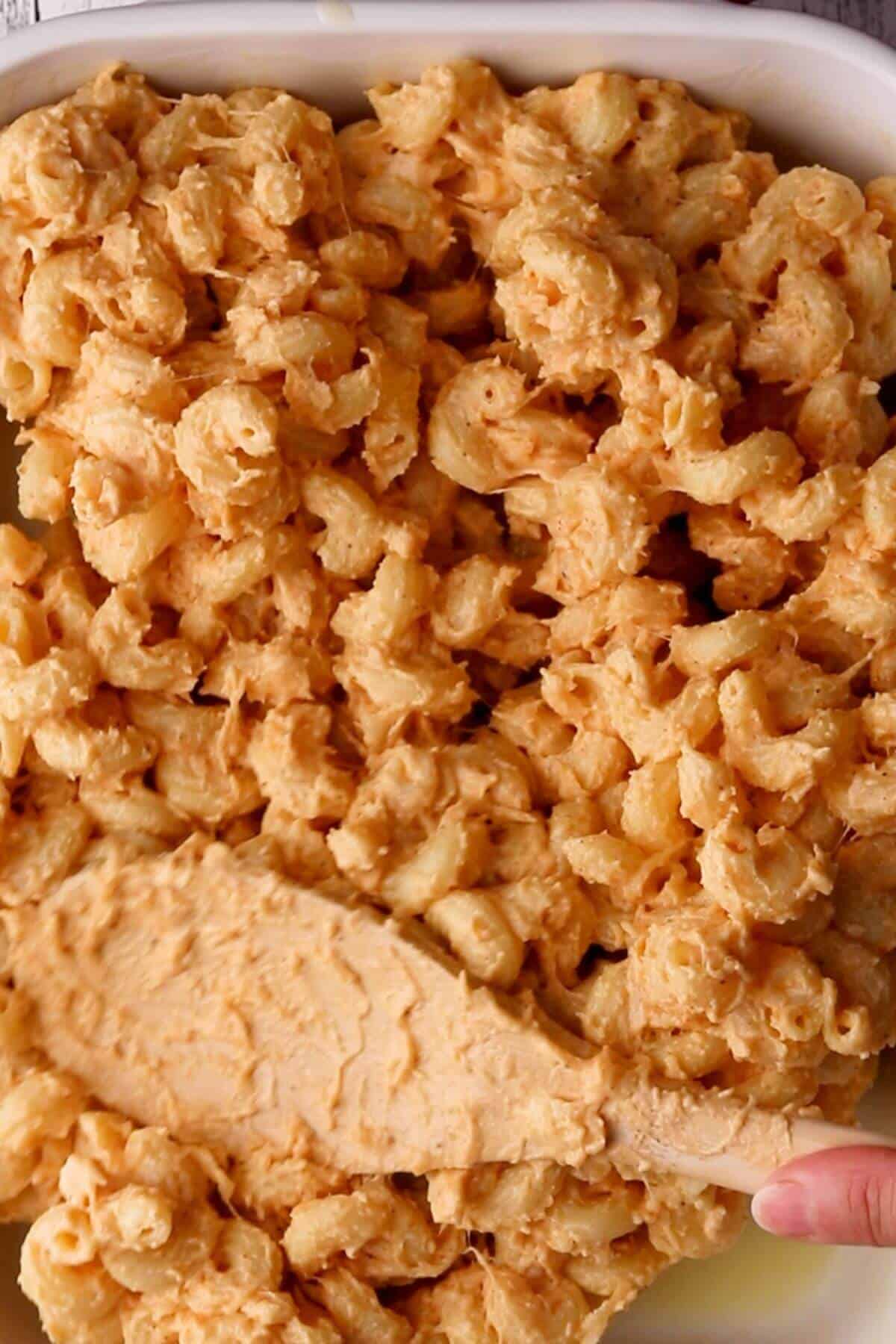 Close-up of a dish with baked macaroni and cheese, showing golden-brown crust and a spatula lifting the surface layer.