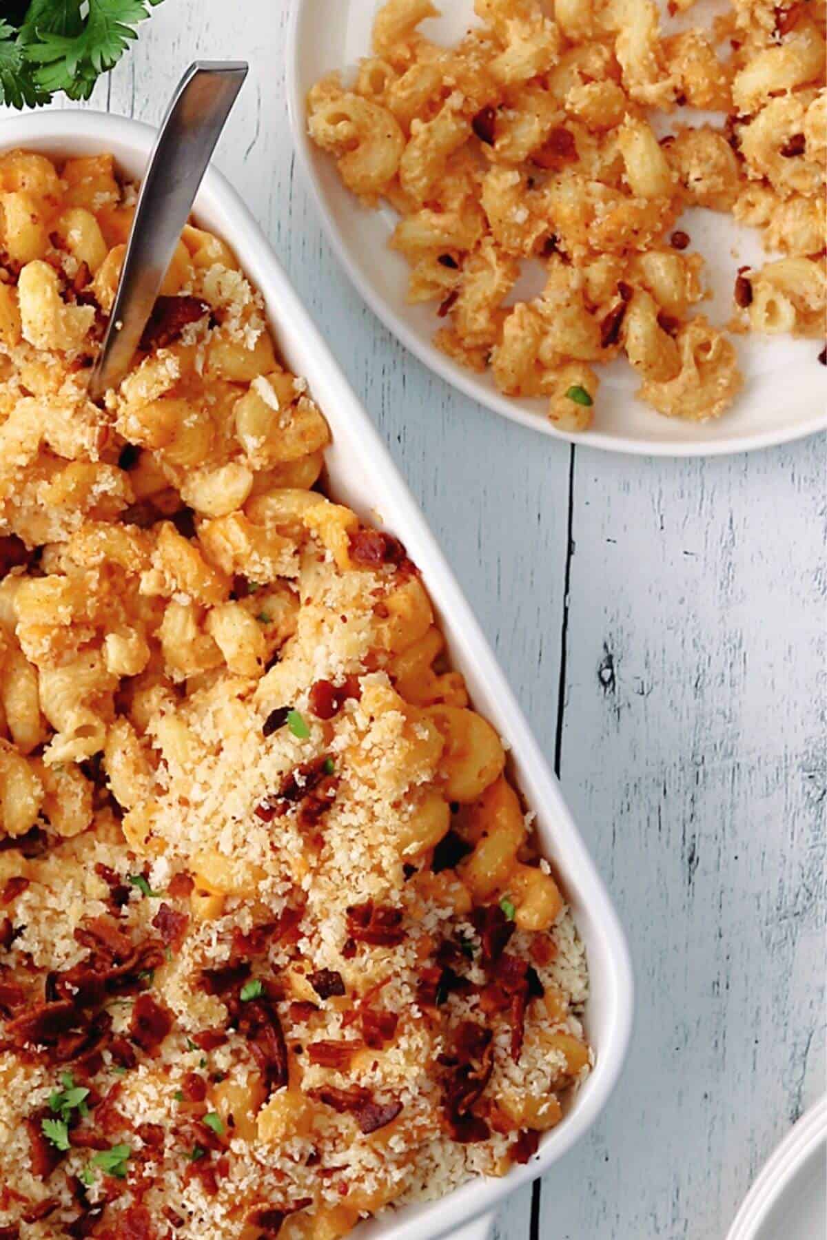 Baked macaroni and cheese topped with breadcrumbs and bacon in a white dish, with a portion served on a plate beside it.