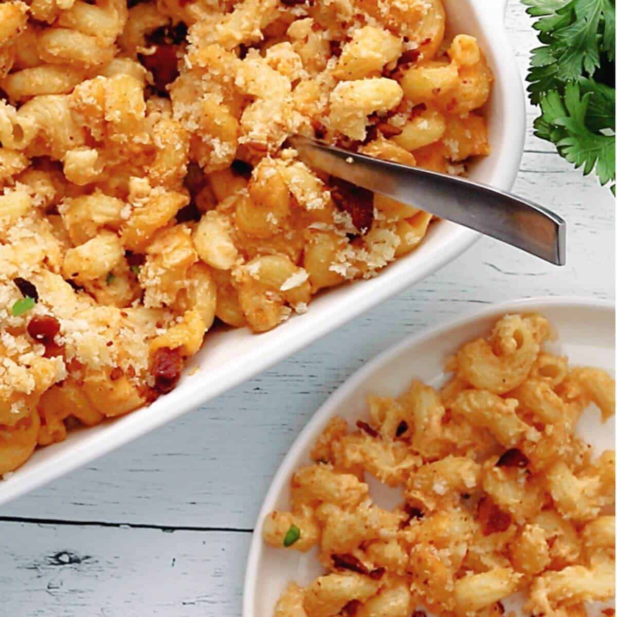 Baked macaroni and cheese with a breadcrumb topping in a casserole dish and a serving on a plate, garnished with parsley.