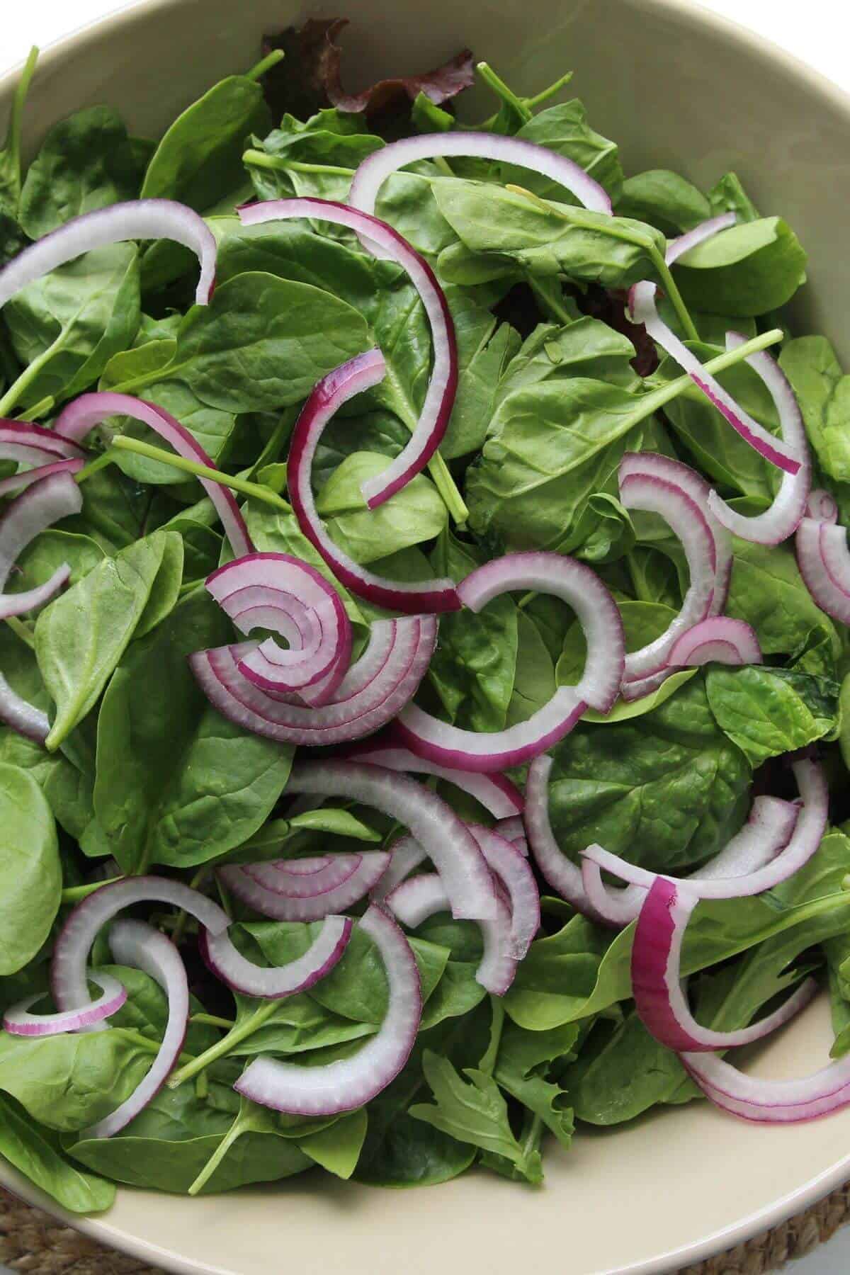 A bowl of fresh spinach leaves topped with sliced red onions.